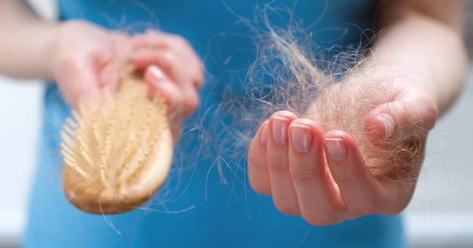 Woman checking hair shedding while brushing in a bathroom mirror