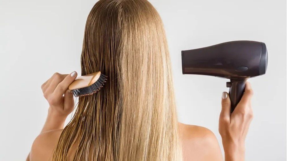 Woman drying hair with a hair dryer — dermatologists warn about daily heat damage
