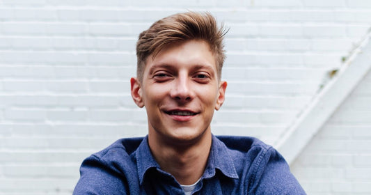 Portrait of a young man against a white brick wall, representing men's haircare.