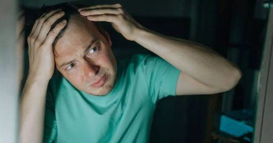 Young man examining scalp in a mirror, concerned about hair thinning