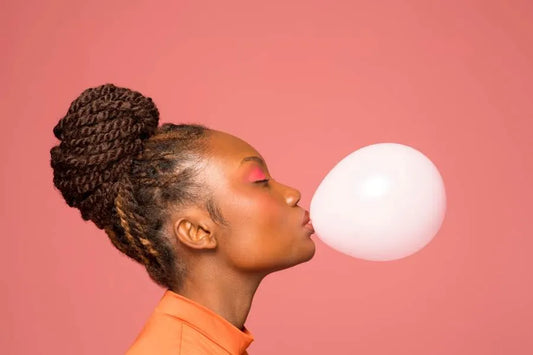 Woman with long, styled hair blowing a bubble with chewing gum