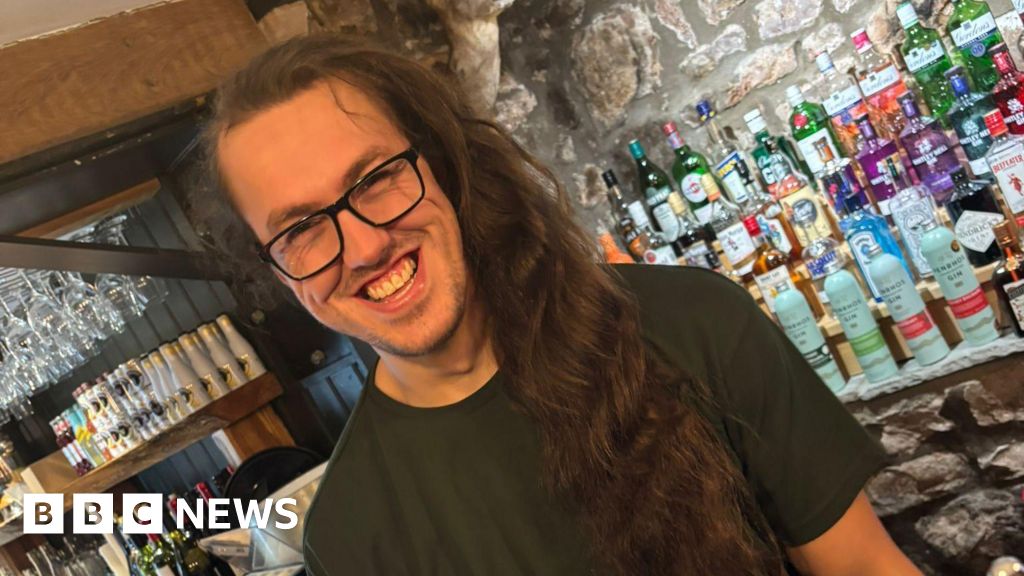 A man with long hair prepares to have it cut for charity